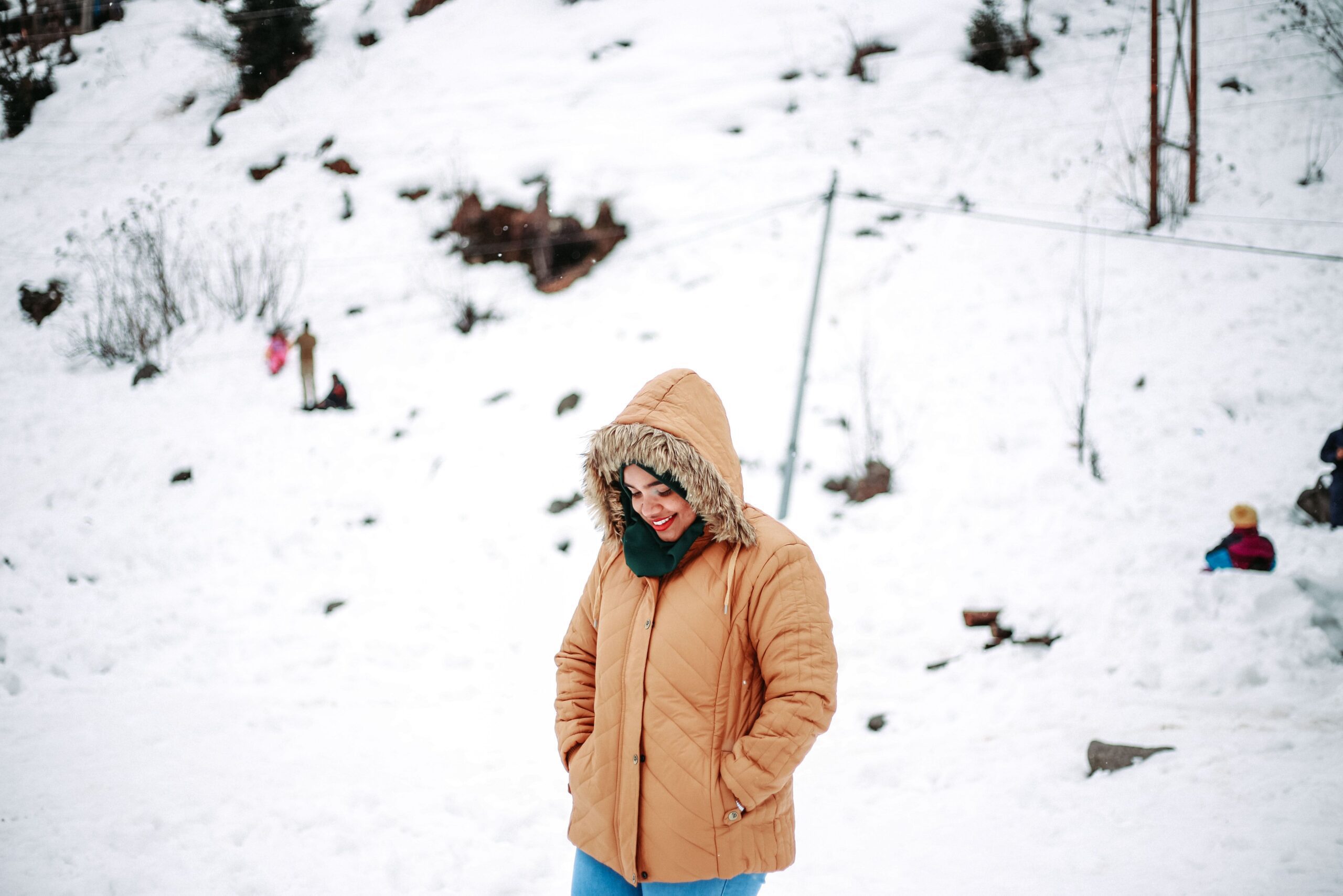 Smiling woman in a brown jacket amid snowy landscape in Manali, India.