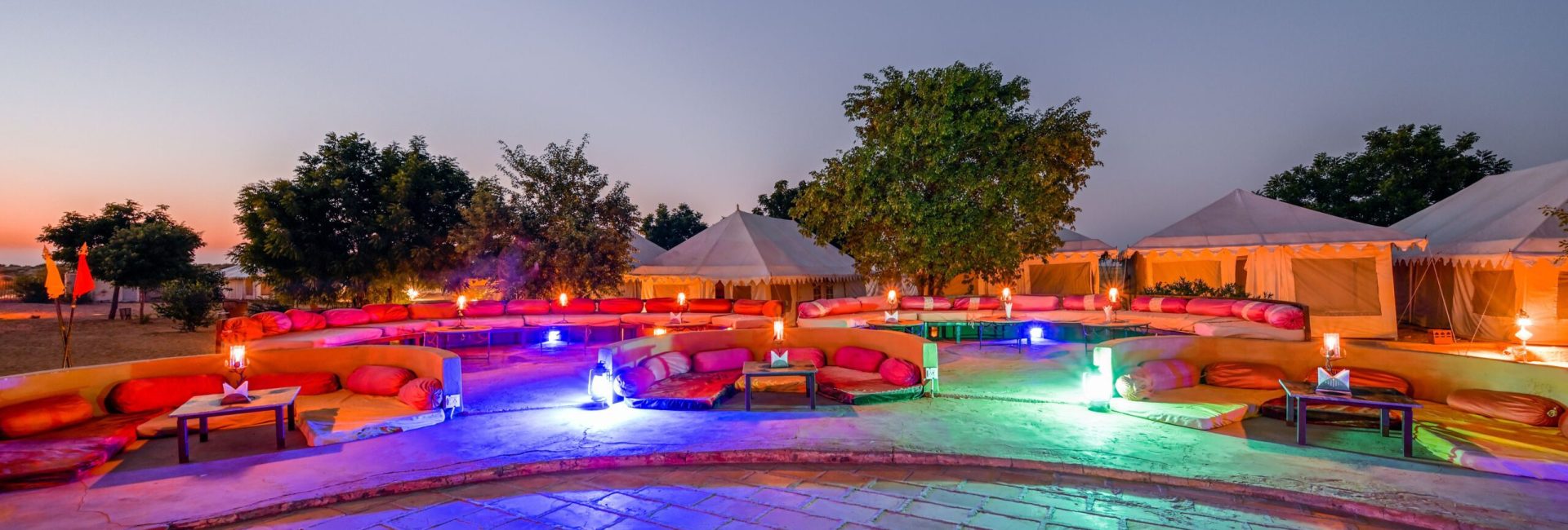 Elegant desert camp in Jaisalmer at dusk, featuring vibrant seating and illuminated tents.